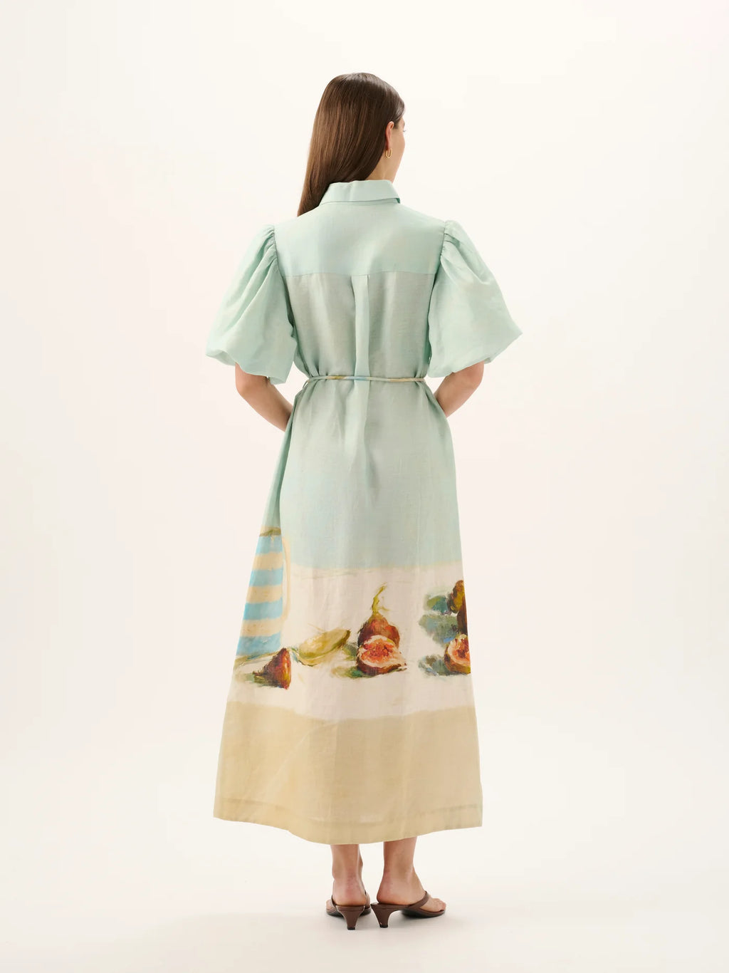 Woman wearing a light green dress with a scenic print on a white background