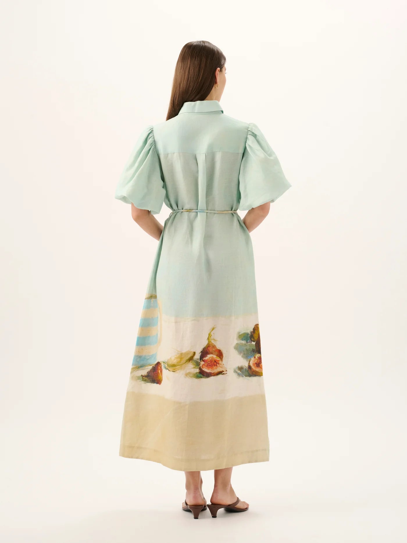 Woman wearing a light green dress with a scenic print on a white background
