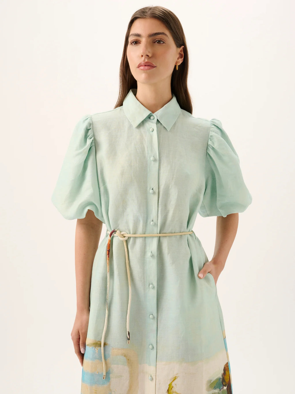 Woman wearing a light green dress with puff sleeves and a colorful patterned skirt on a white background