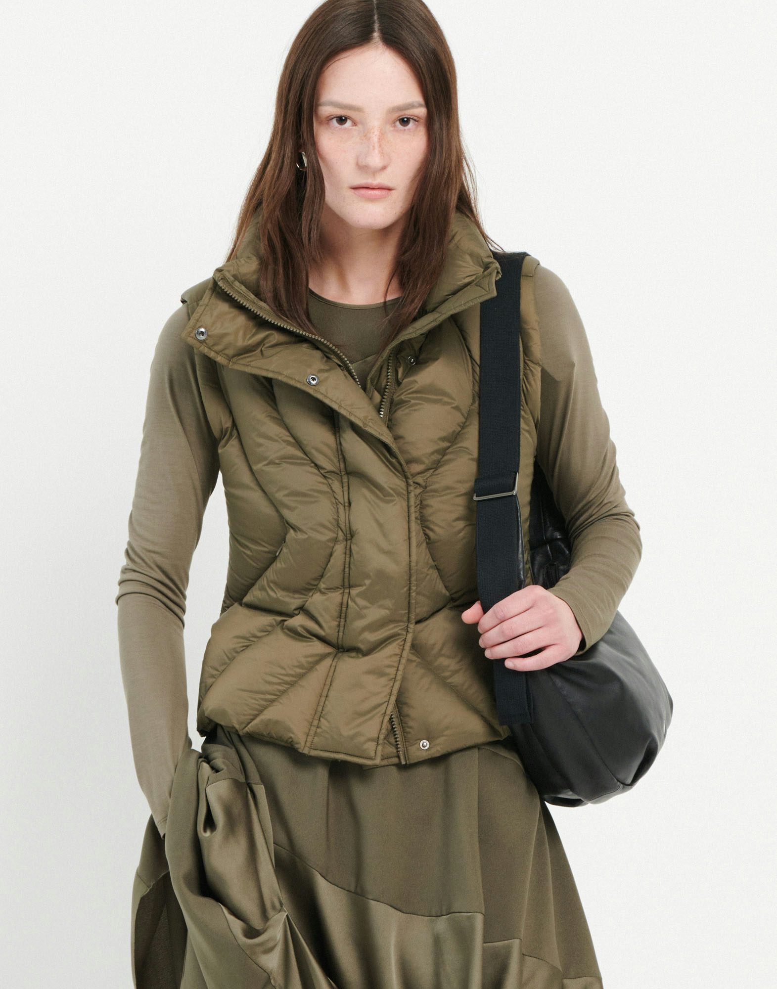 Woman wearing a green puffer jacket holding a black bag on a white background