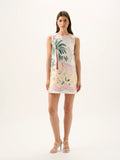 Woman wearing a sleeveless dress with palm tree and flamingo design on a white background