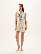 Woman wearing a sleeveless dress with palm tree and flamingo print on a white background
