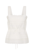 An off-white eyelet cotton camisole top with wide shoulder straps, a square neckline, horizontal gathered detailing, a drawstring tie at the waist, and a scalloped eyelet hem.