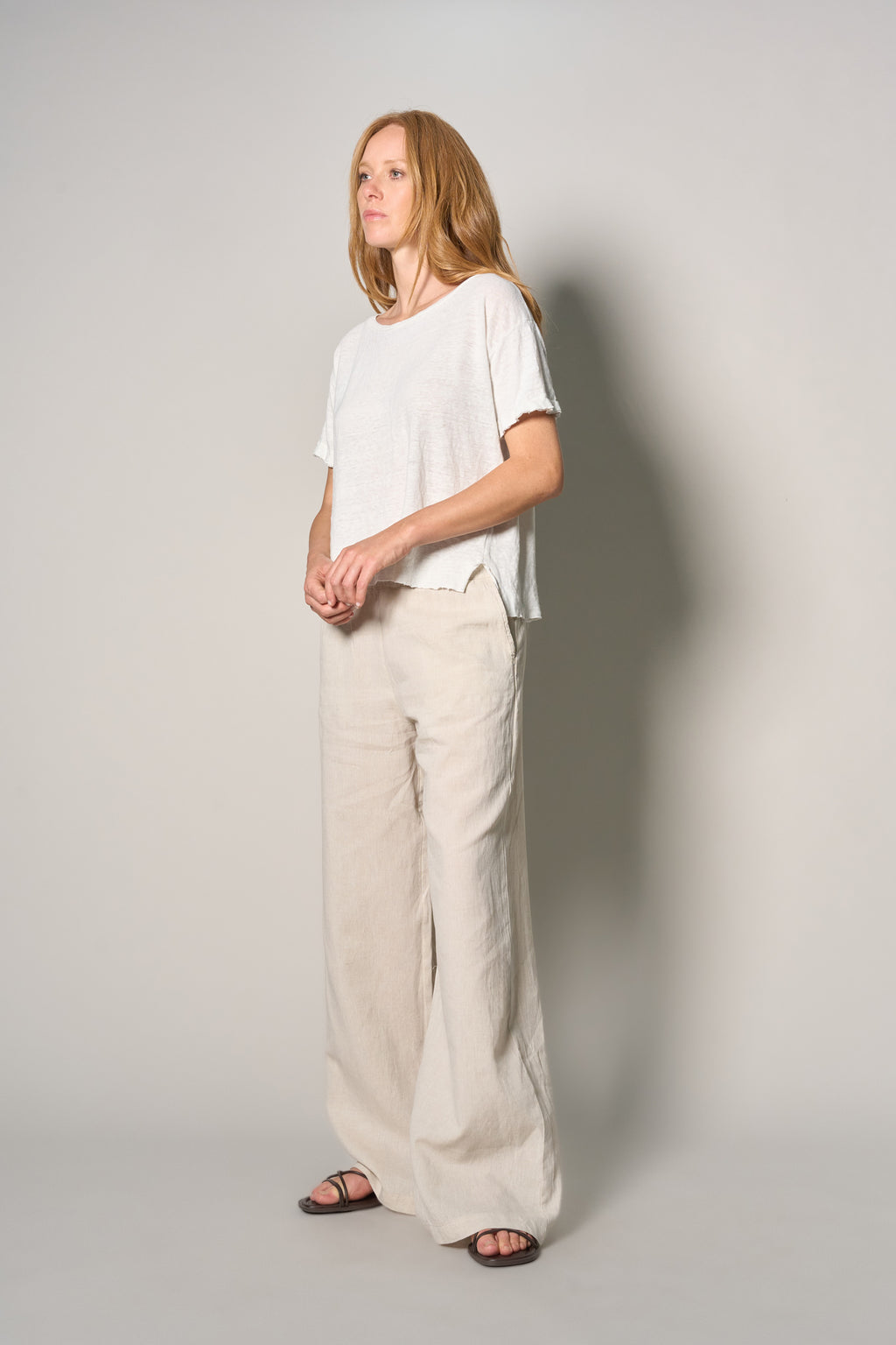 A woman modeling a white short-sleeve top and wide-leg beige trousers against a plain light gray studio background.