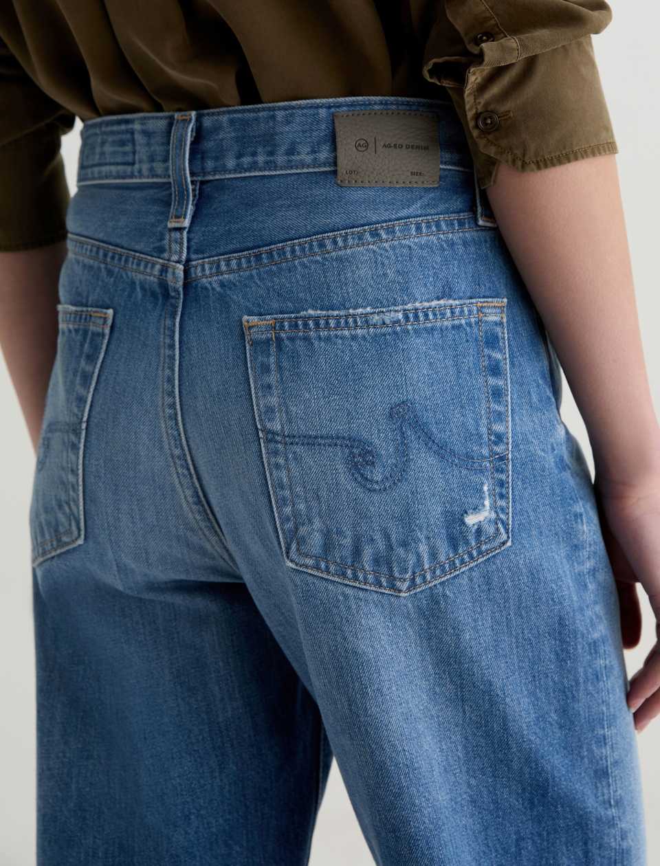 Blue jeans with a brand label on the back pocket against a neutral background