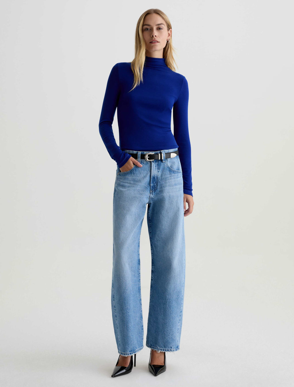 Woman wearing a blue turtleneck and jeans on a white background