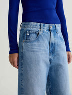 Person wearing blue jeans and a blue long-sleeve shirt on a light background