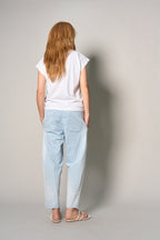 A woman with long red hair is shown from behind wearing a white t-shirt, light blue relaxed-fit jeans, and white flat sandals against a plain light gray studio background.