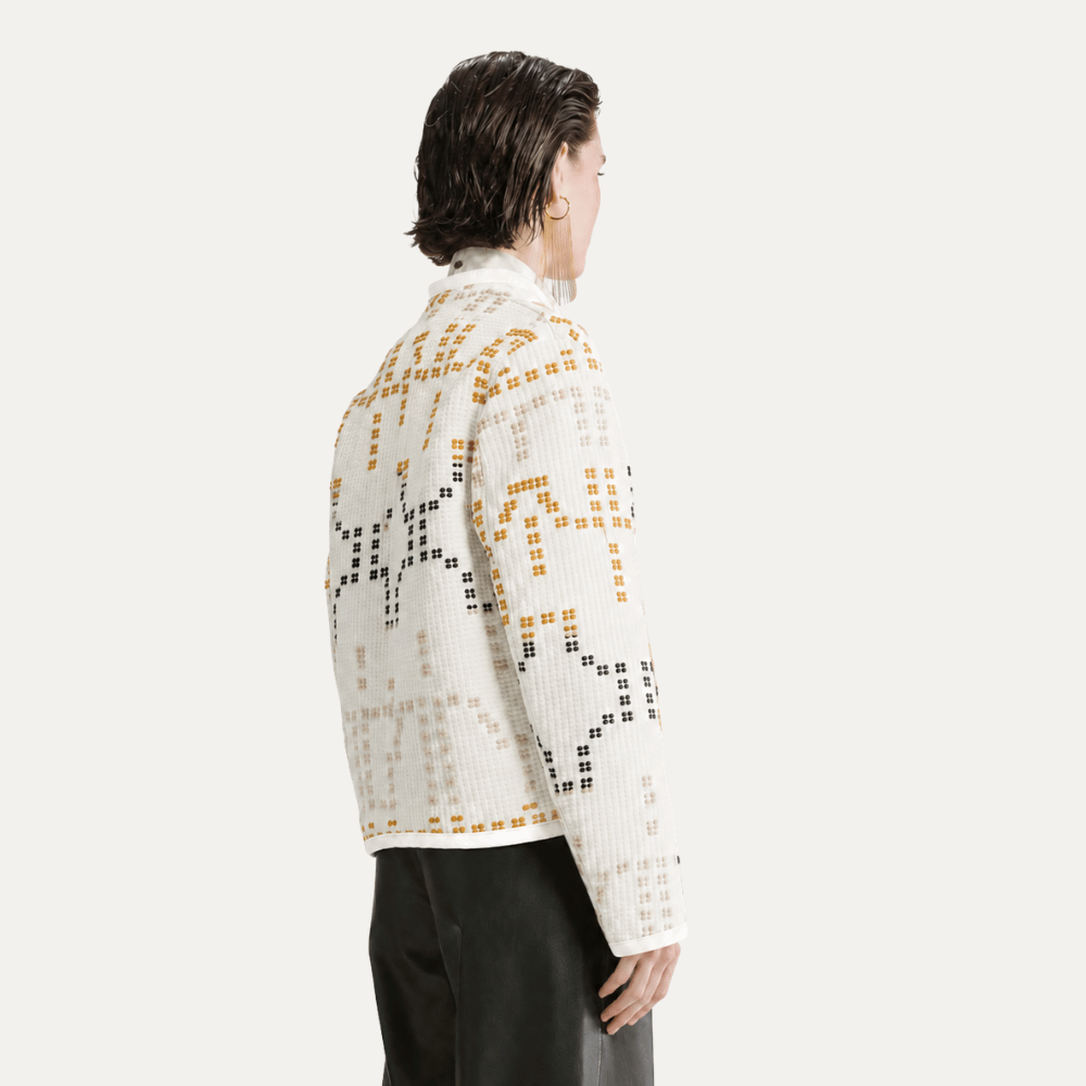A model shown from the back wearing a white knit cropped cardigan with a geometric pattern of black and mustard yellow squares, paired with dark trousers, against a light gray studio background.