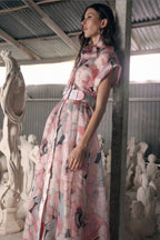 A woman wearing a floral bridal bouquet gown with short sleeves, a pussy bow neck detail, and a full skirt standing in a room with sculpture molds in the background.