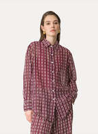 A woman wearing a maroon and white geometric patterned oversized shirt with a collar and buttons down the front, paired with matching pants.
