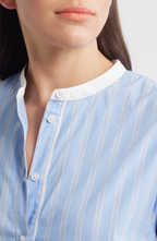 A close-up of a woman wearing a blue and white striped shirtdress with long sleeves and a band collar.