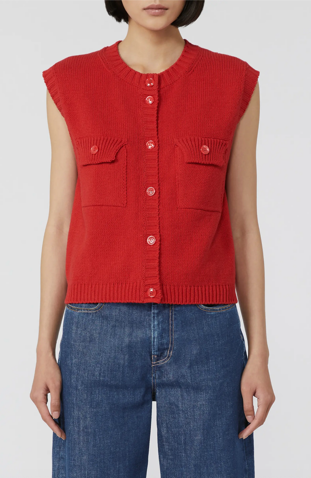 Person wearing a red sleeveless knitted vest and blue jeans on a white background