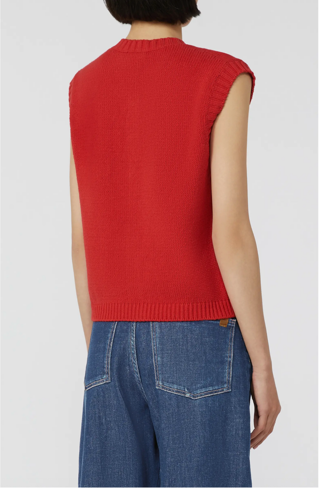 Person wearing a red sleeveless sweater over a blue denim outfit on a white background