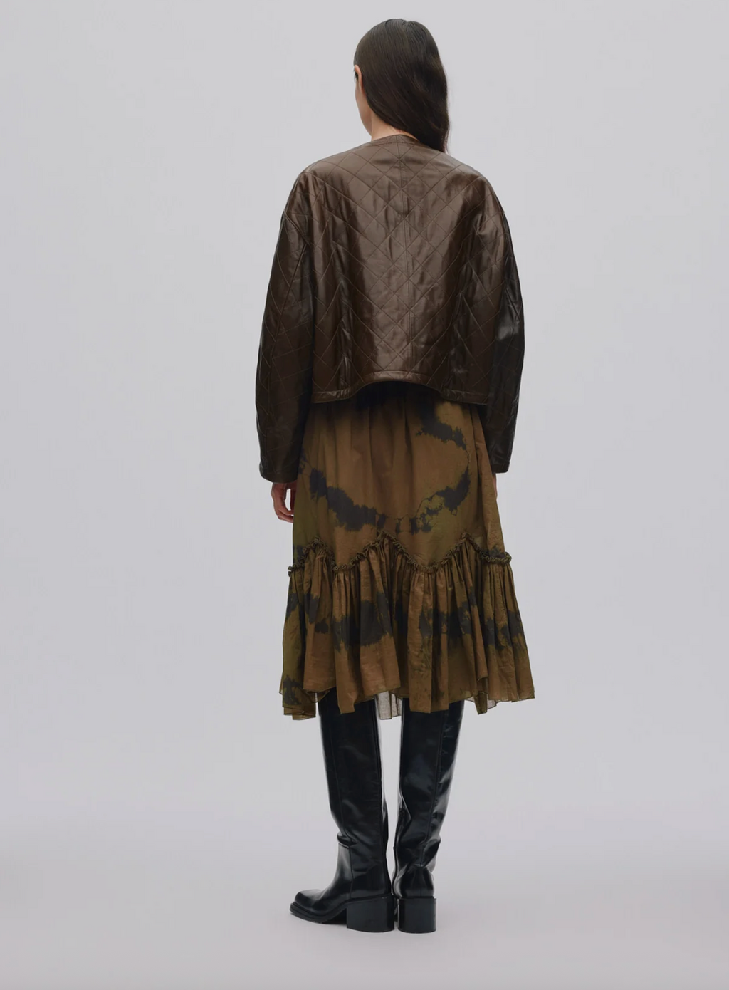 Person wearing a long, dark brown coat with a patterned skirt on a white background