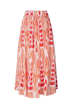 A high-waisted, flared midi skirt featuring a vibrant orange and coral-red ikat-style pattern on a white base, shown against a light gray studio background.