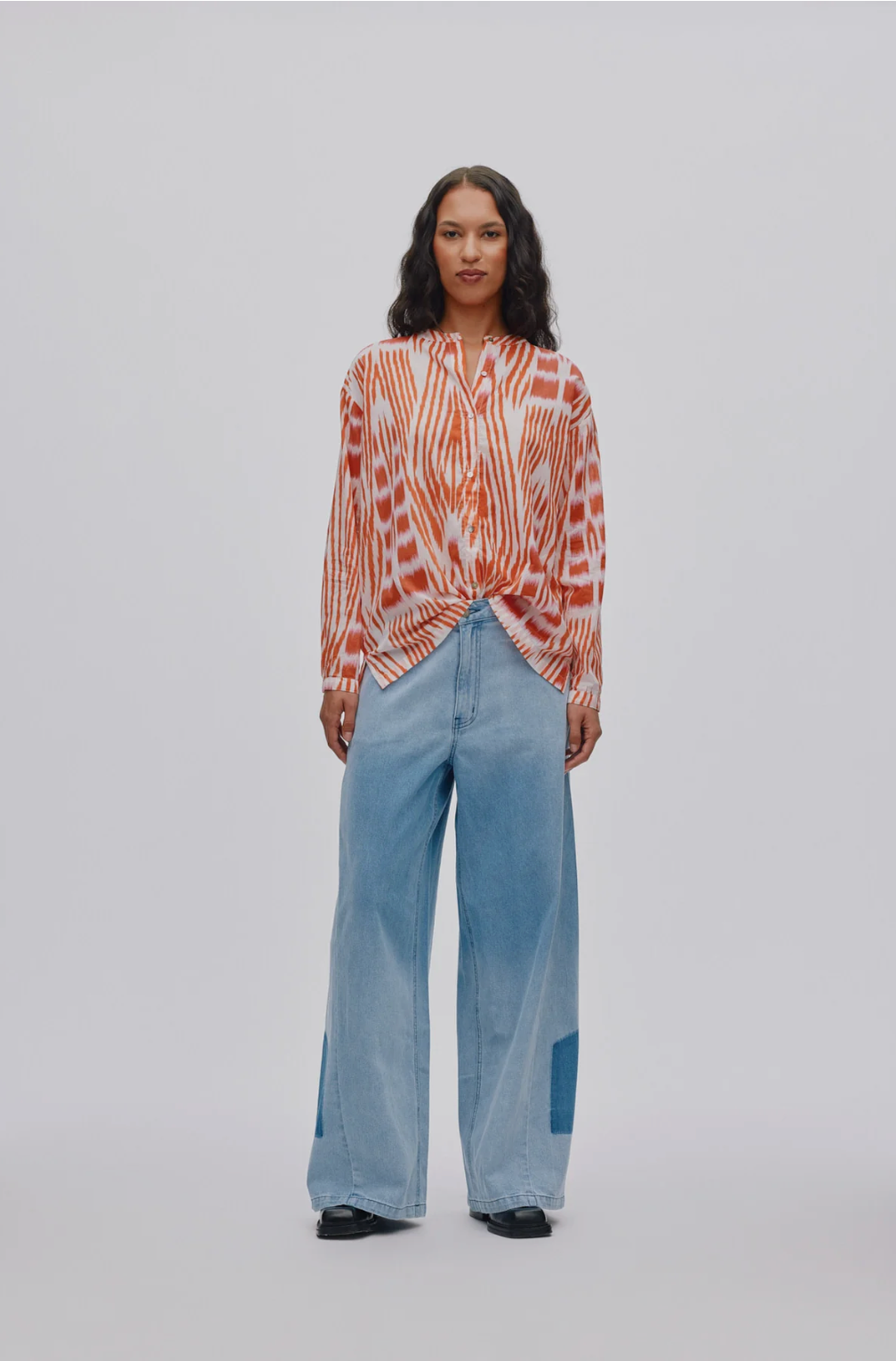 Woman wearing a patterned blouse and light blue jeans on a white background