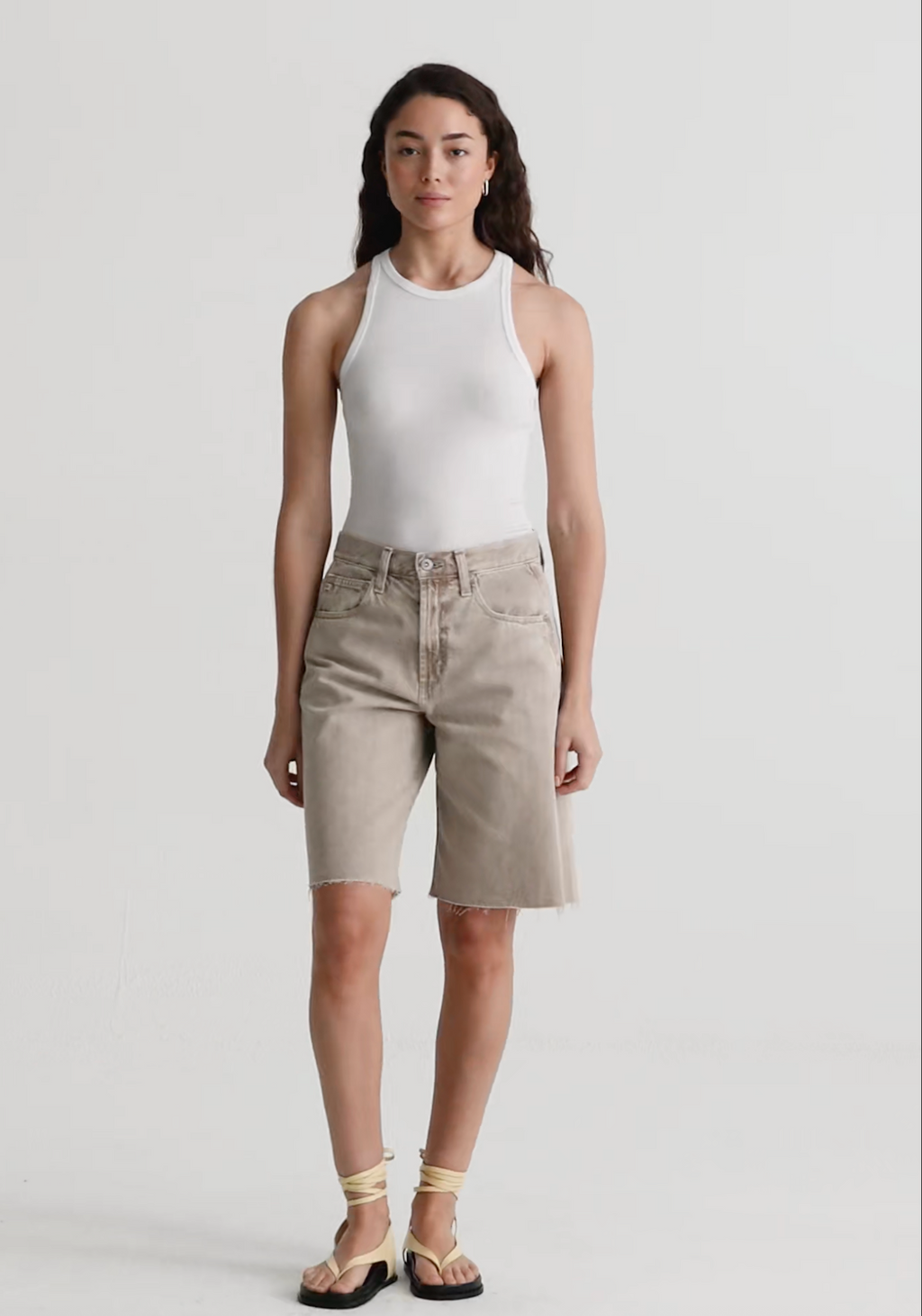 Woman wearing a white sleeveless top and beige shorts on a plain background