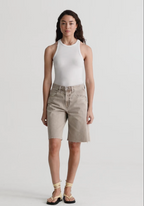 Woman wearing a white sleeveless top and beige shorts on a plain background