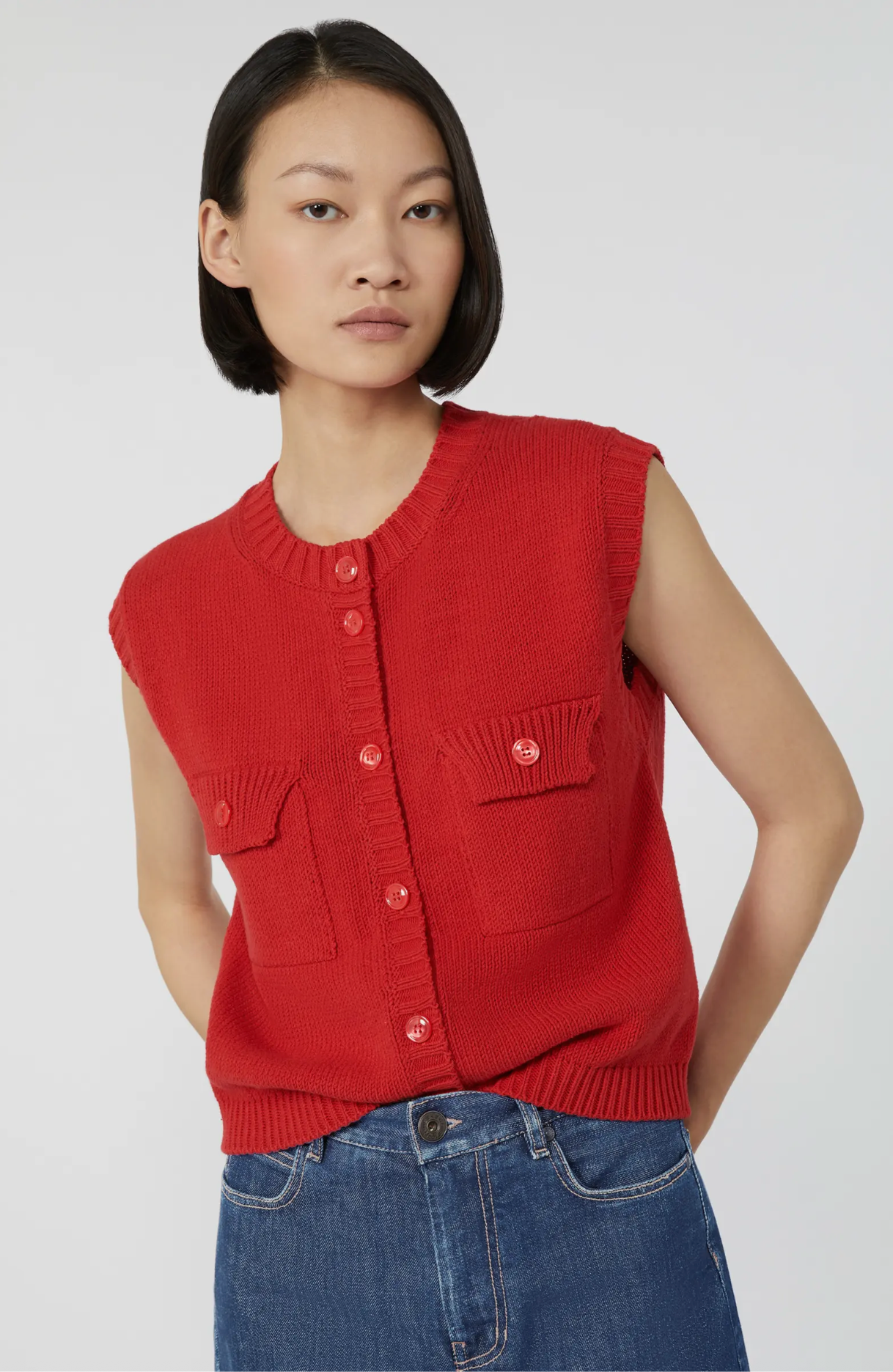 Woman wearing a red sleeveless cardigan and blue jeans on a white background