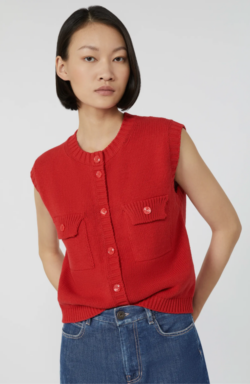 Woman wearing a red sleeveless cardigan and blue jeans on a white background
