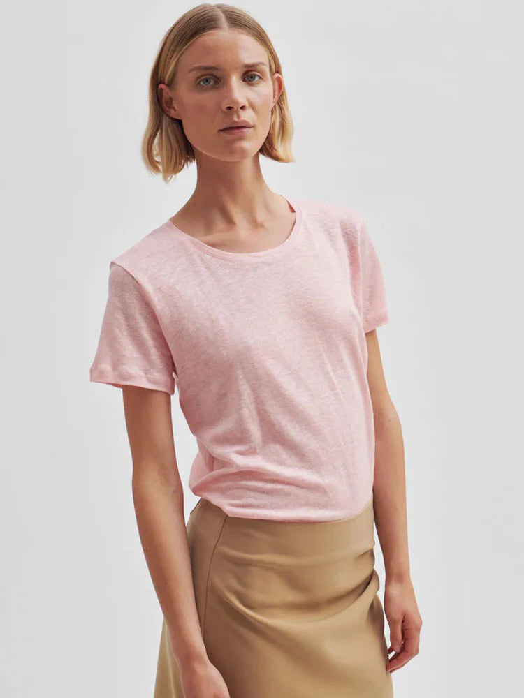 Woman wearing a second female pink linen t-shirt and beige pants against a plain background