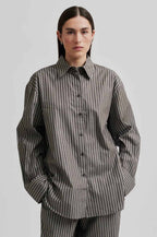 A model wearing a Second Female Saka Mulch Shirt, which is a striped, long-sleeved shirt with a button front fastening and a collar. The shirt appears to be made of cotton and is presented in a black and gray color palette.