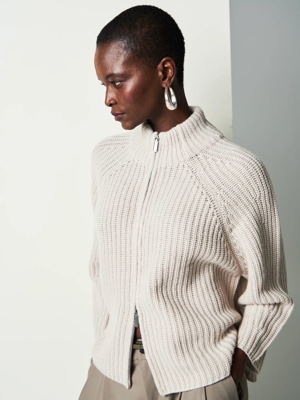Person wearing a beige ribbed sweater against a plain background