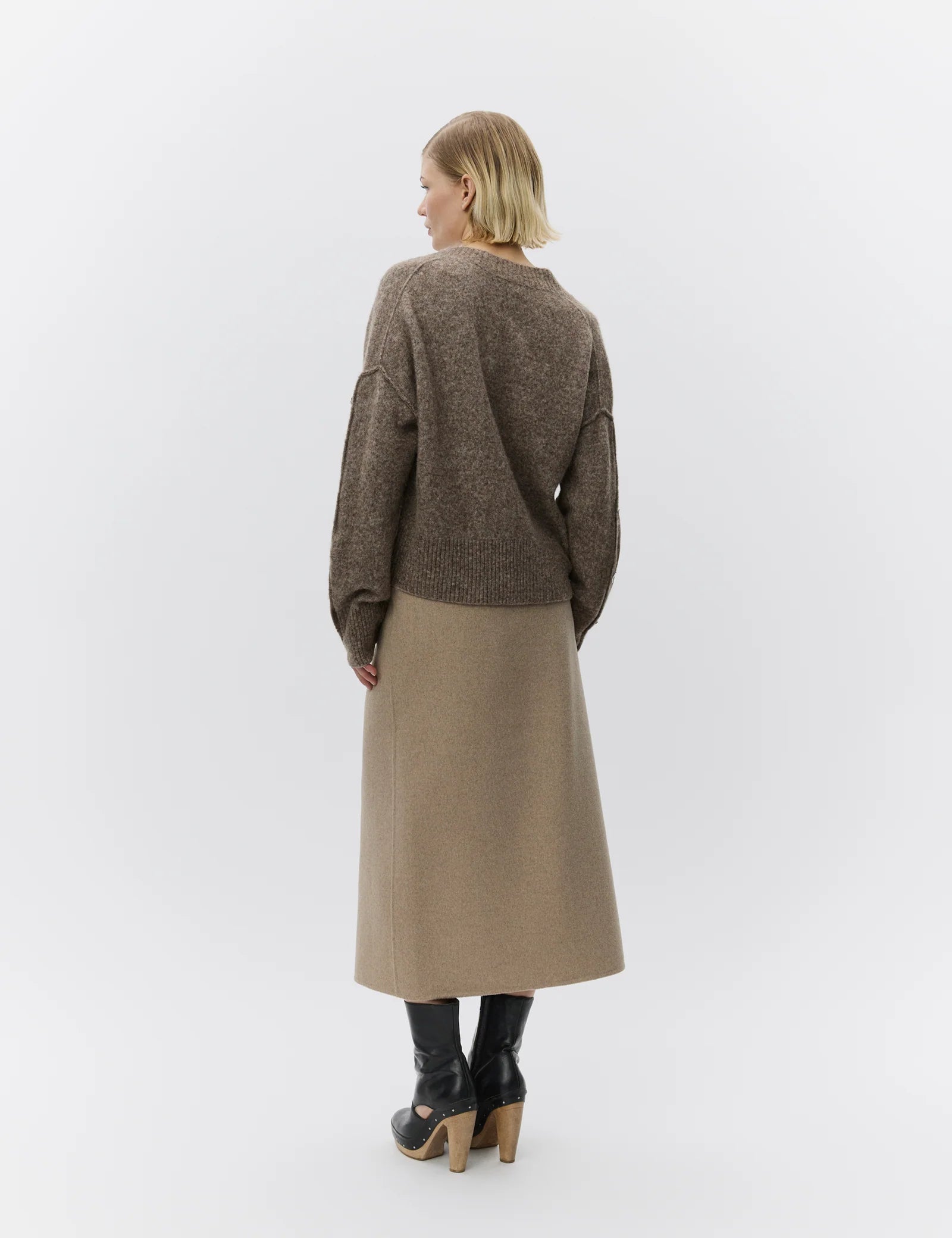 Person wearing a brown sweater and beige skirt against a white background