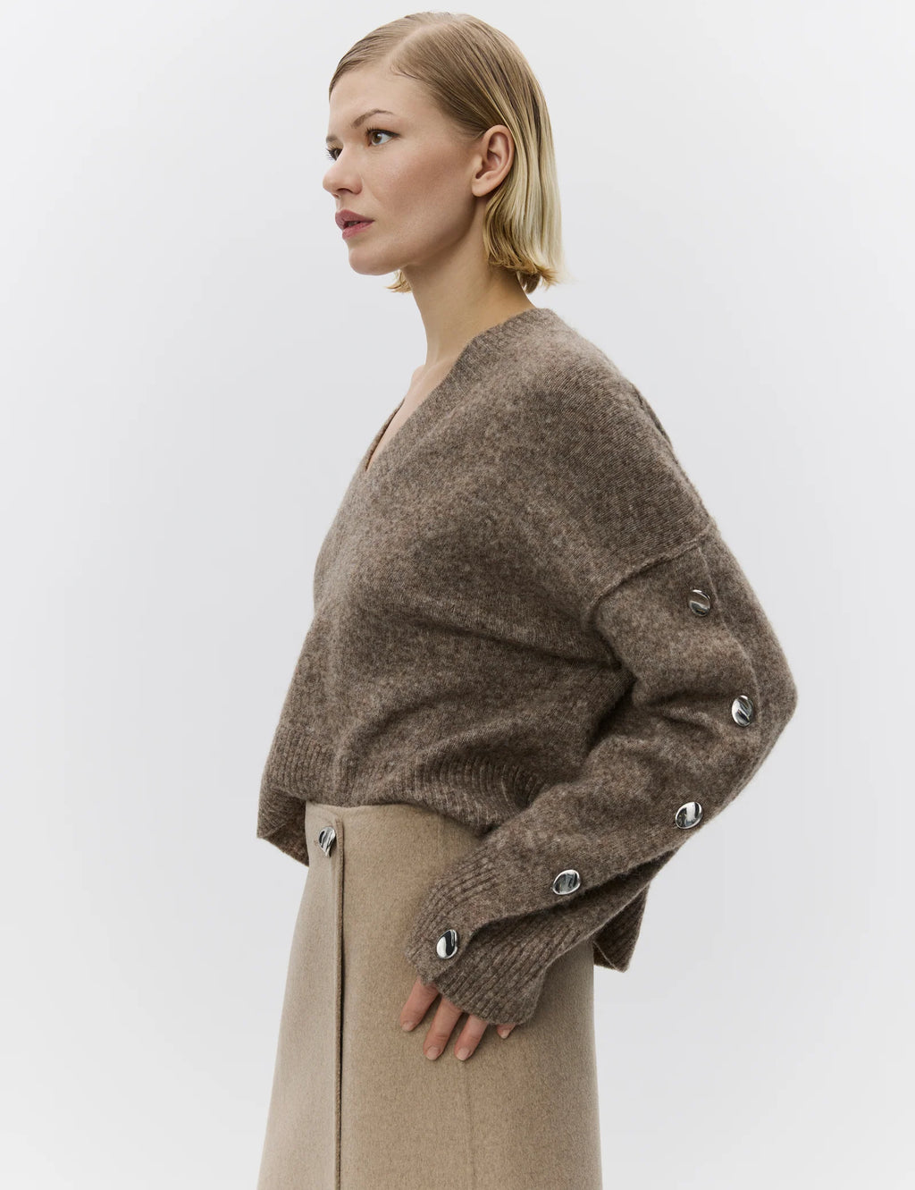 Woman wearing a brown sweater with button details on a white background