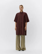 Person wearing a brown shirt and green pants on a white background