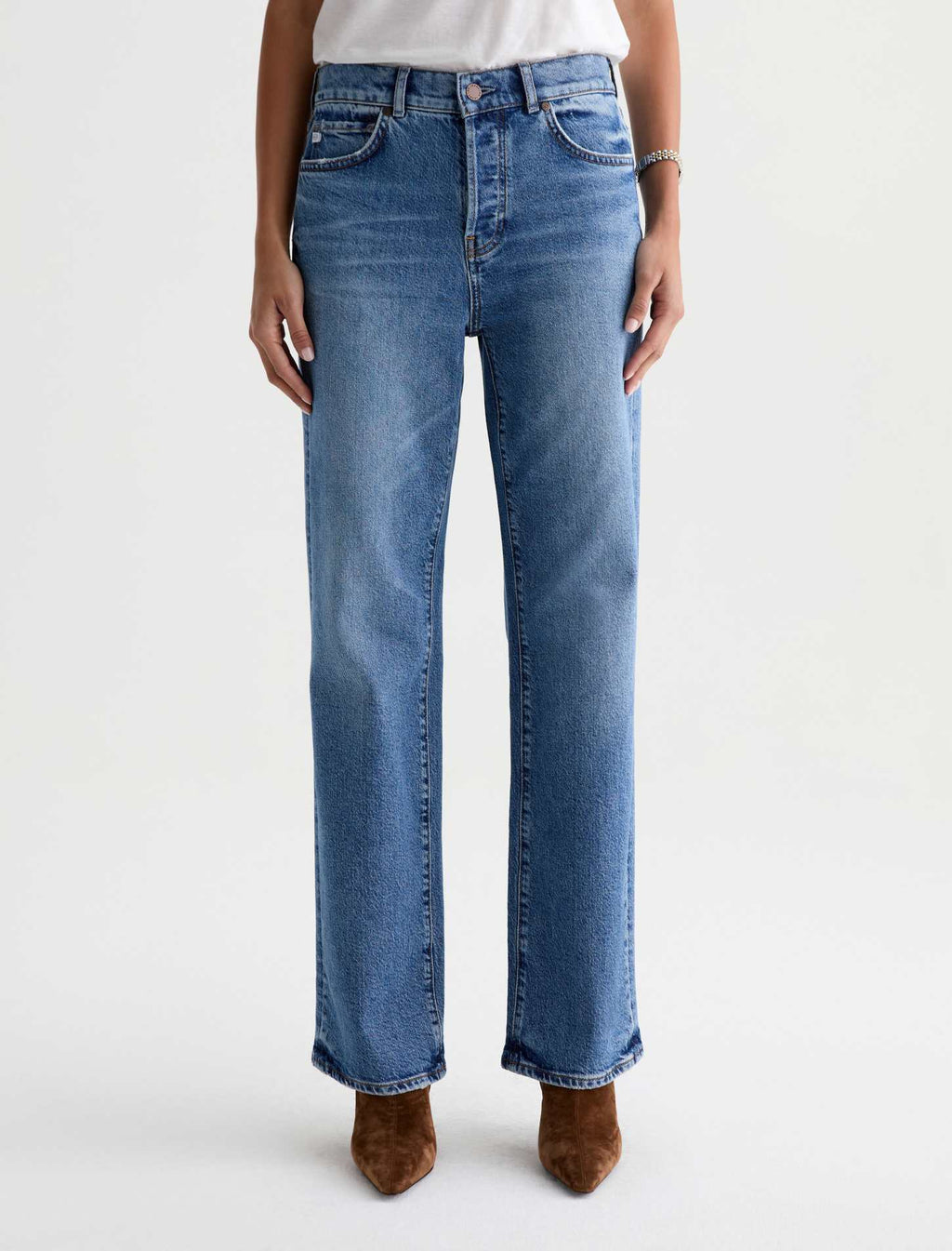 A person wearing medium-wash blue straight-leg jeans with brown pointed-toe boots, shown from the waist down against a plain light gray studio background.