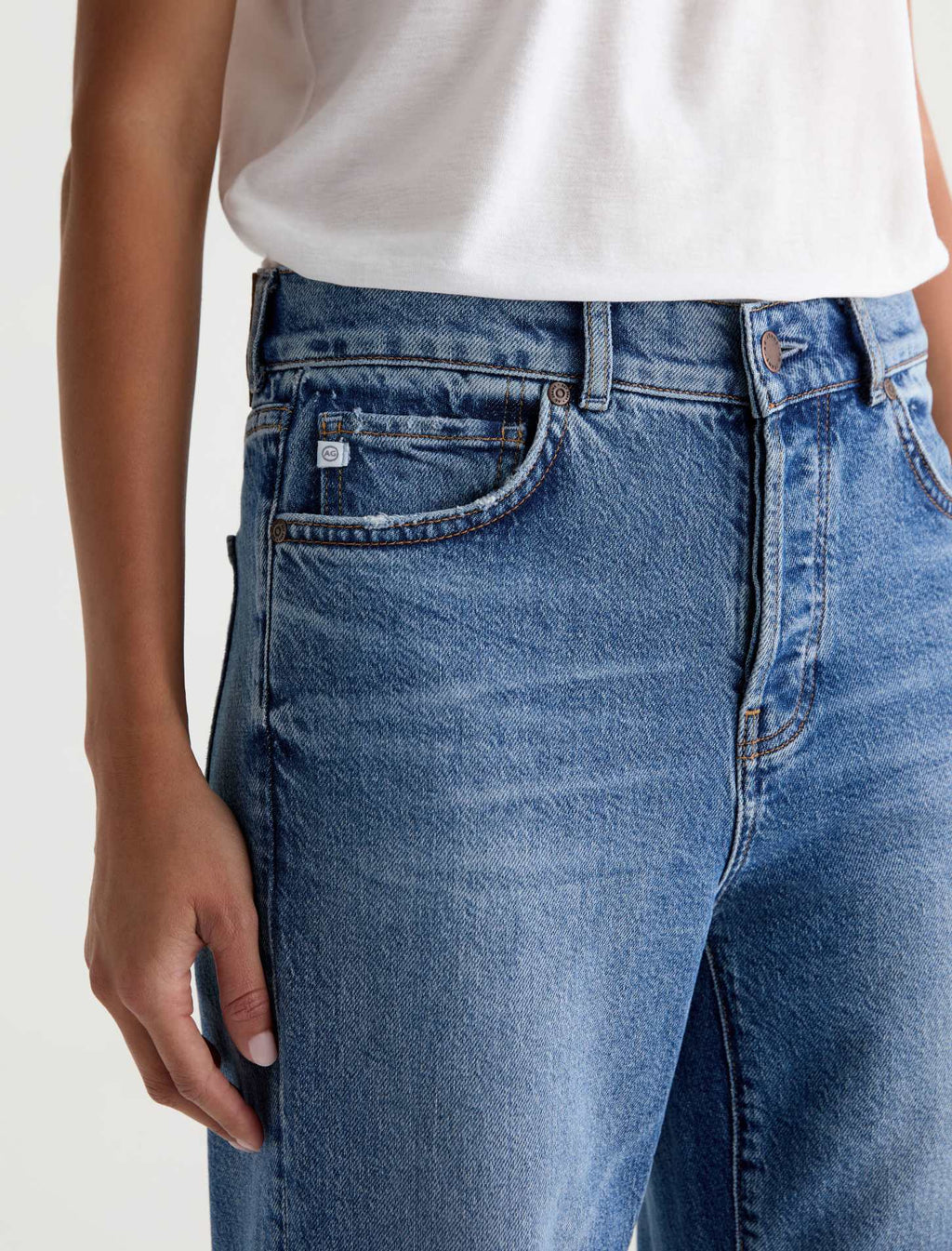 Close-up of a person wearing medium-wash blue denim jeans with a white top, showing the front pocket and waistband area.