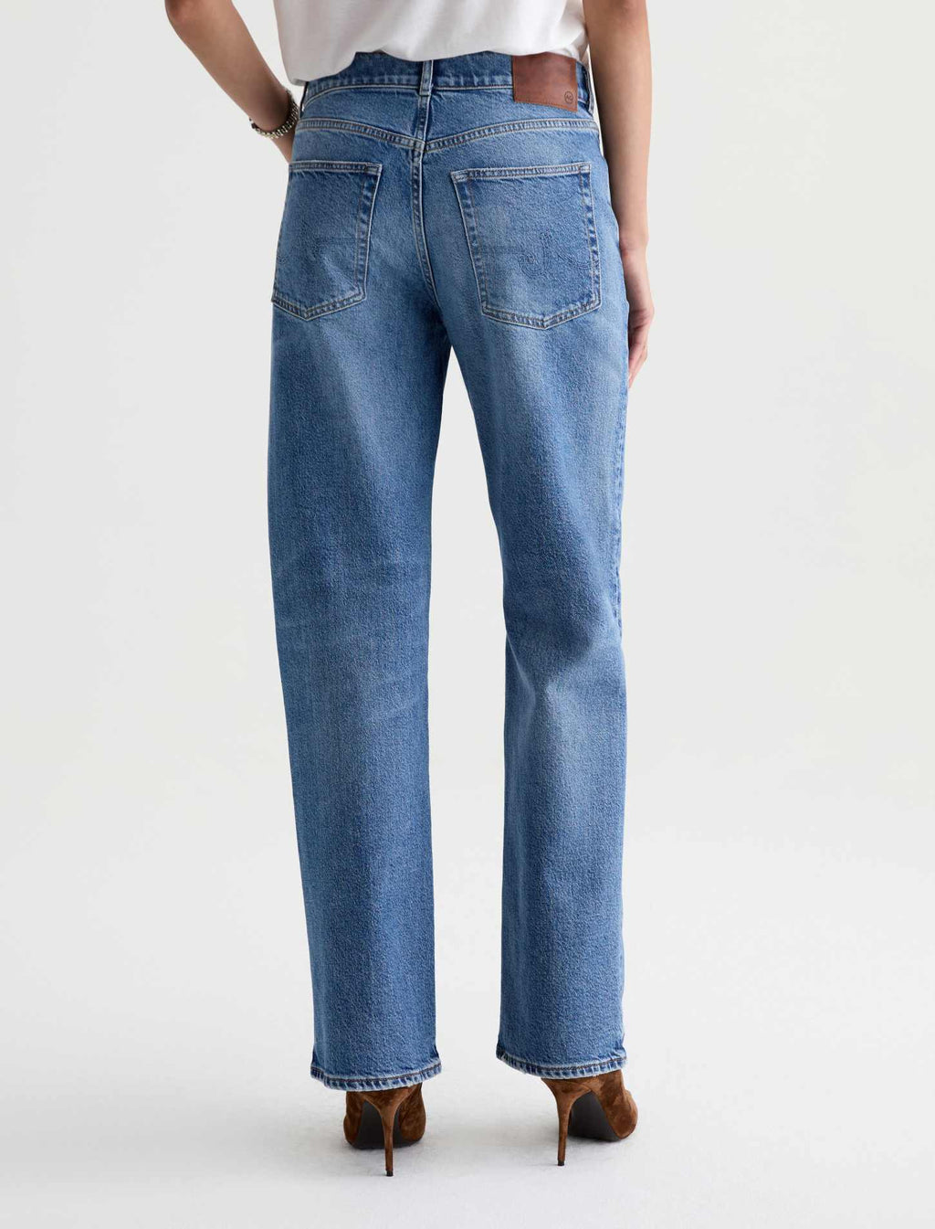 Rear view of a person wearing light blue straight-leg denim jeans with brown high heels against a clean white studio background.