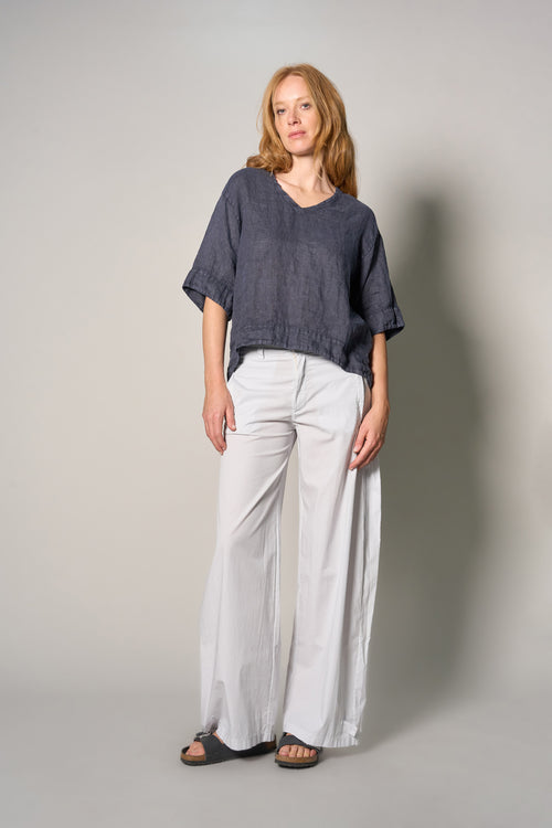 A woman modeling a loose, short-sleeve dark gray linen top and wide-leg light gray pants, standing against a neutral gray studio background.