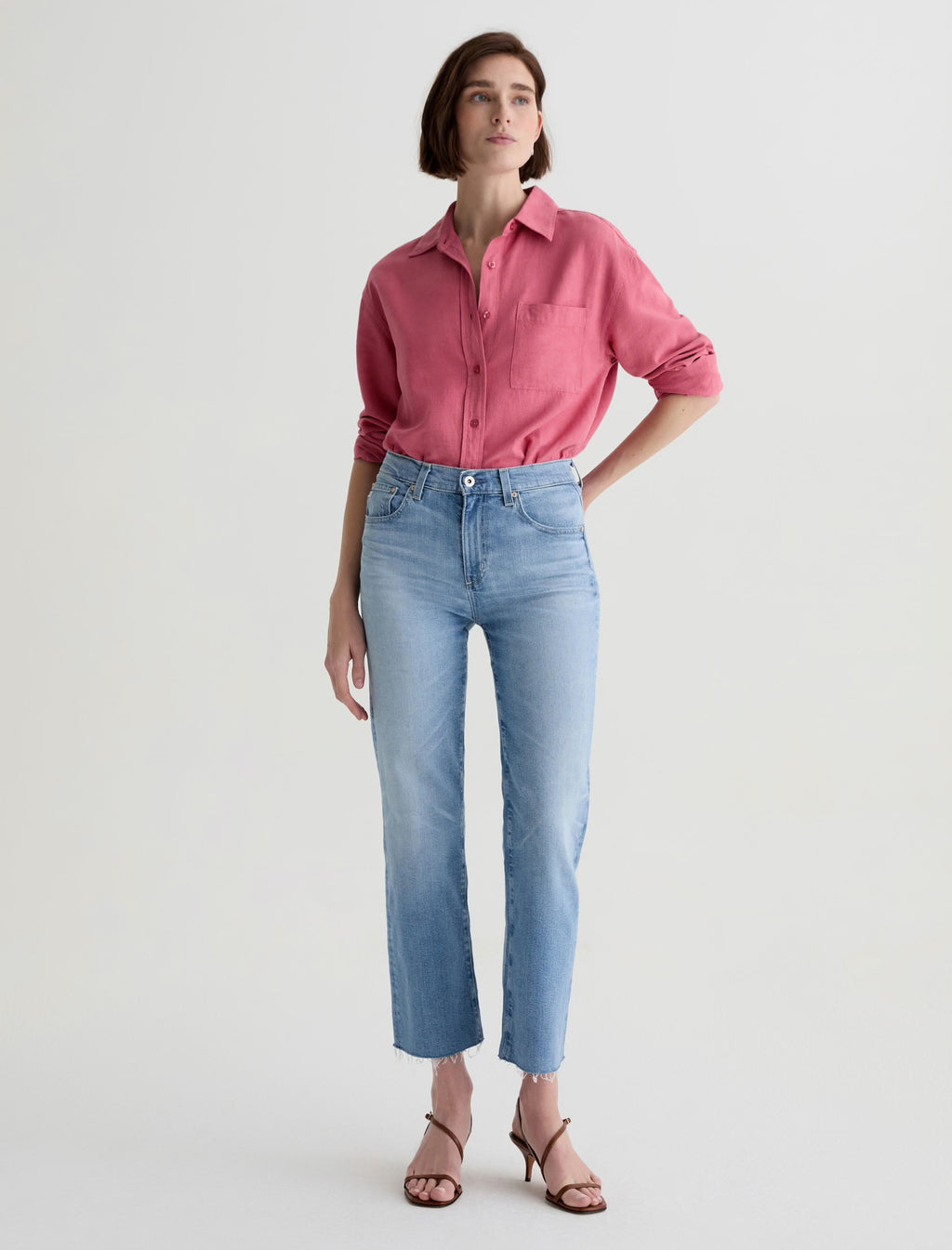 Woman wearing a pink shirt and light blue Brinley Crop Fiction AG jeans on a white background front side.shop online