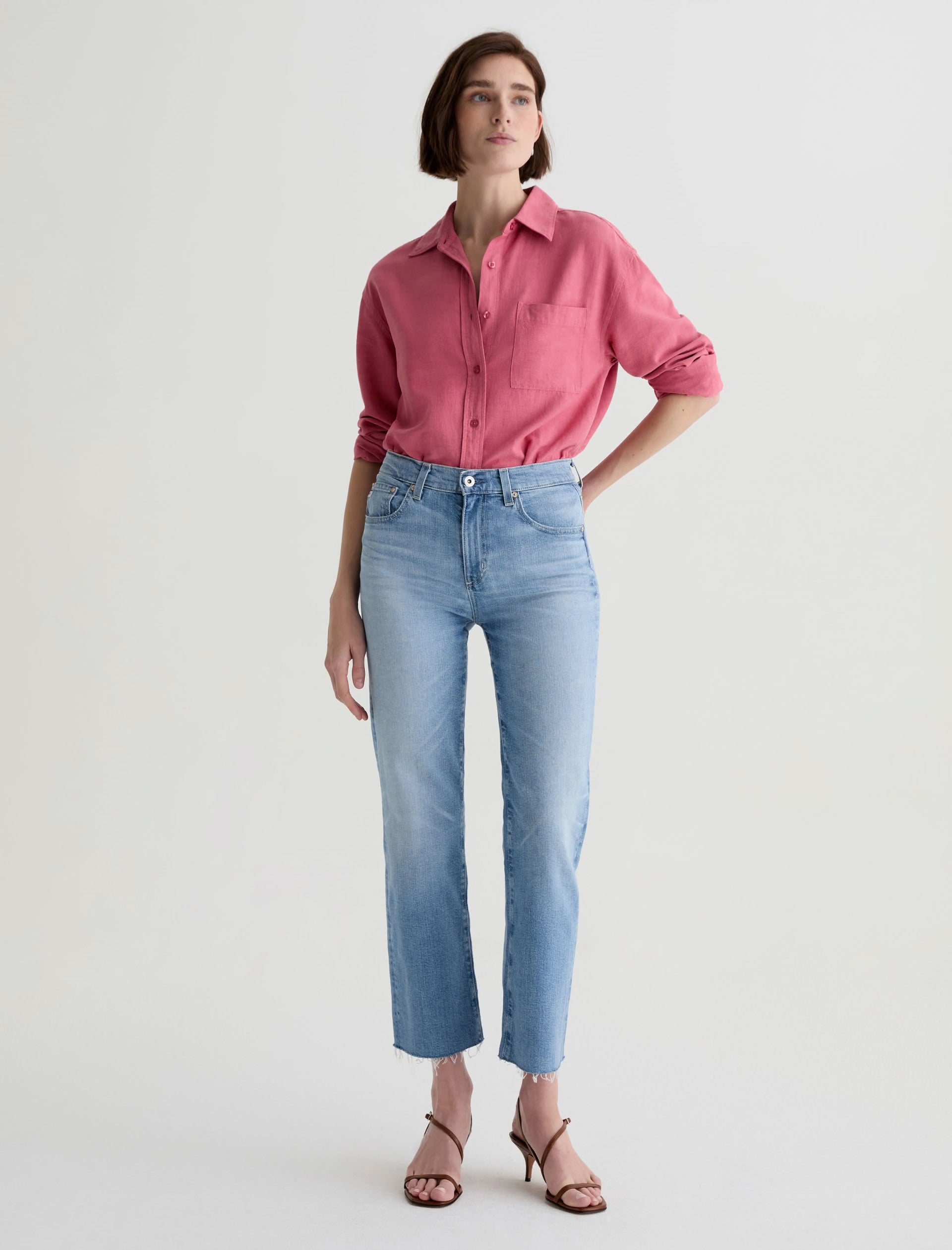Woman wearing a pink shirt and light blue Brinley Crop Fiction AG jeans on a white background front side.shop online
