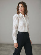 Woman wearing a white lace blouse and black pants against a plain background