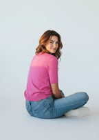 Woman wearing a pink shirt and blue jeans sitting on a white floor.