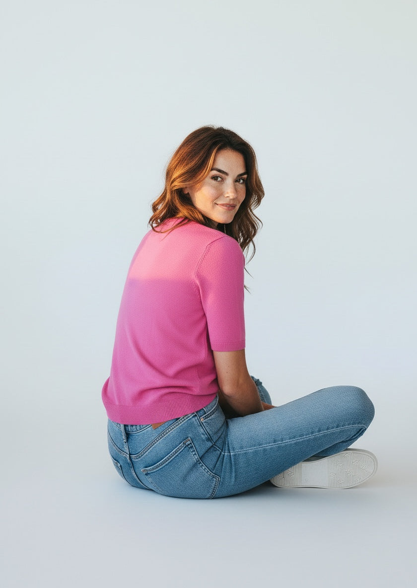 Woman wearing a pink shirt and blue jeans sitting on a white floor.