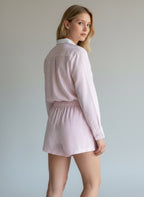 Woman wearing a light pink striped shirt and shorts set against a plain background