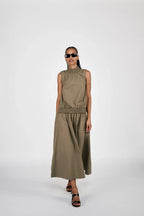 Woman wearing a sleeveless olive green top and long skirt on a white background