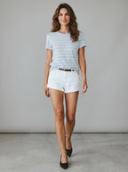 Woman wearing a striped shirt and white shorts against a plain background