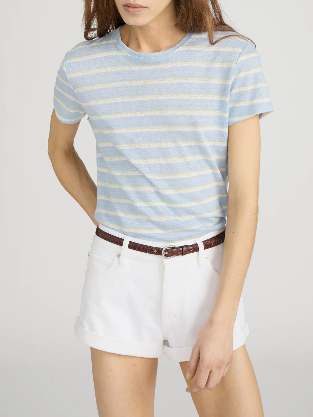 Woman wearing a light blue and yellow striped t-shirt with white shorts on a plain background