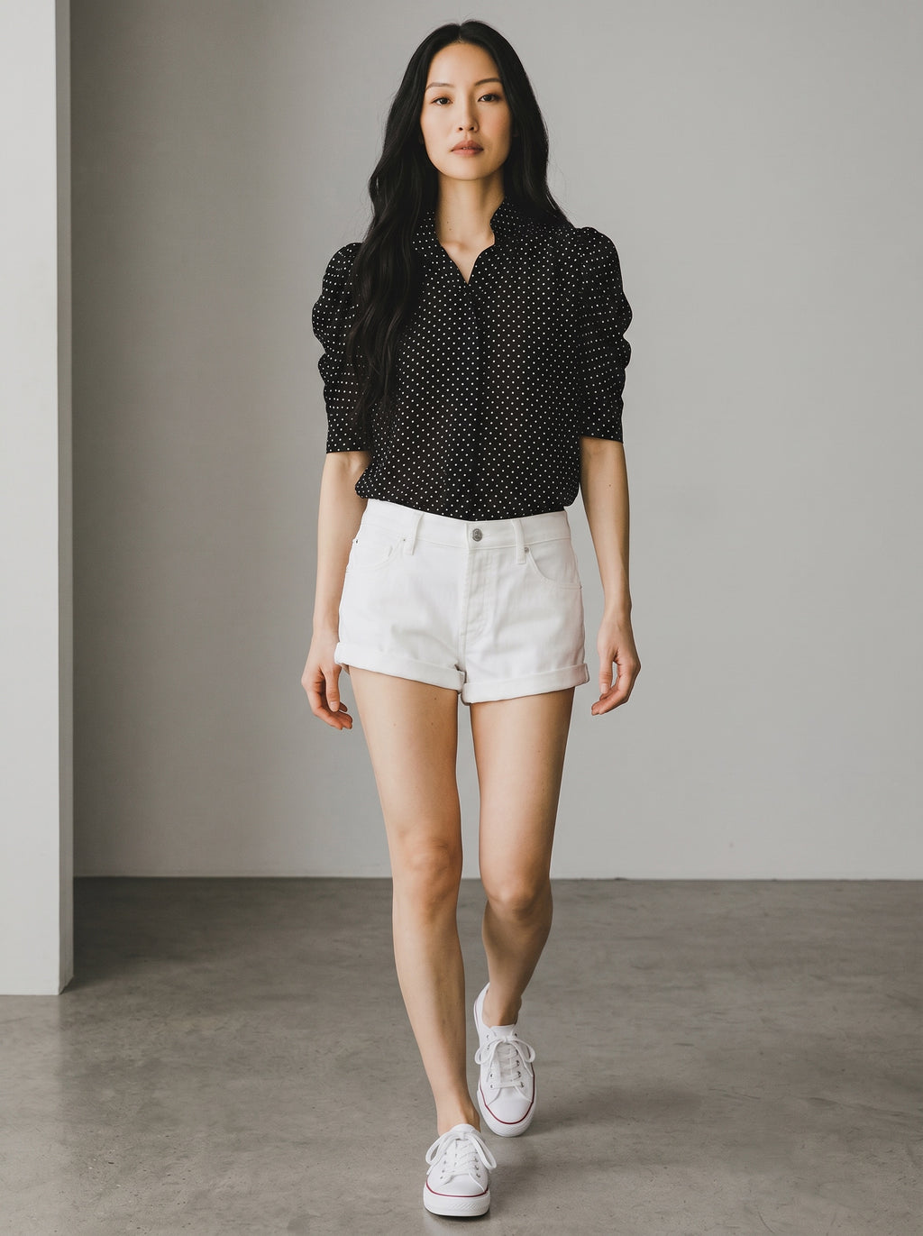 Woman wearing a black polka dot shirt and white shorts against a neutral background