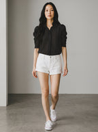 Woman wearing a black polka dot shirt and white shorts against a neutral background