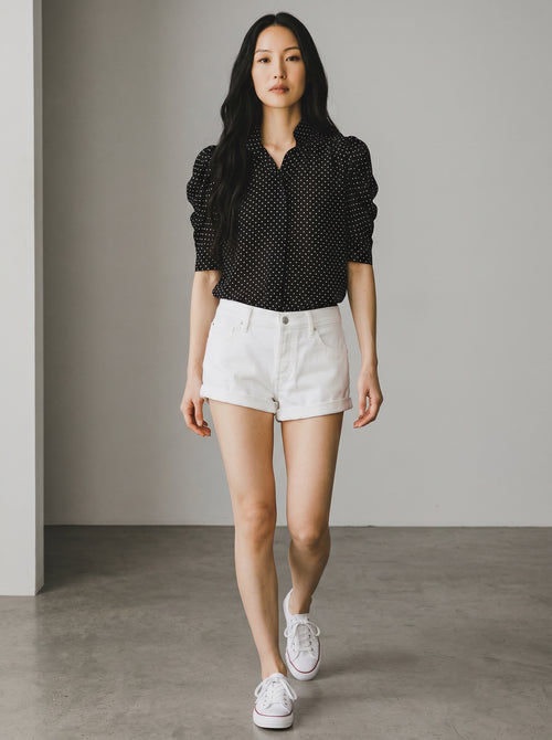 Woman wearing a black polka dot shirt and white shorts against a neutral background