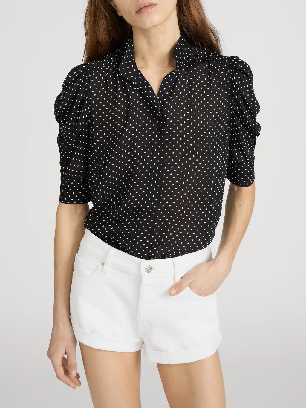 Woman wearing a black polka dot blouse and white shorts on a light gray background