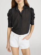 Woman wearing a black polka dot blouse and white shorts on a light gray background