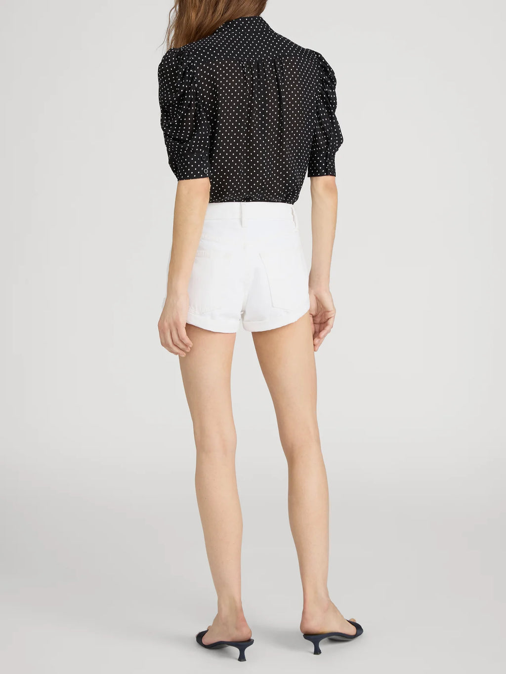 Person wearing a black polka dot blouse and white shorts on a light gray background